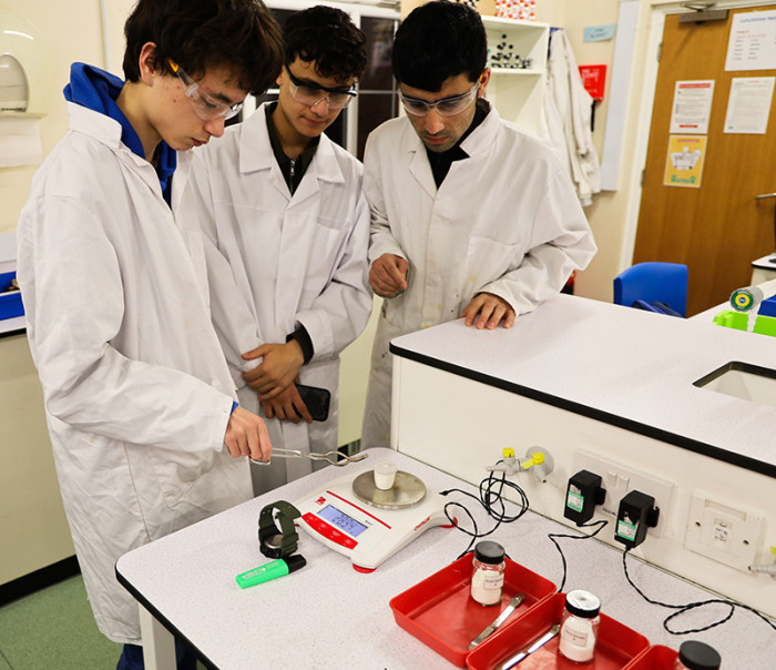 A1 chemistry student Noa (left) shows ESOL students Mohammed and Muhammad how to check whether the mass has stabilised and the reaction has finished.